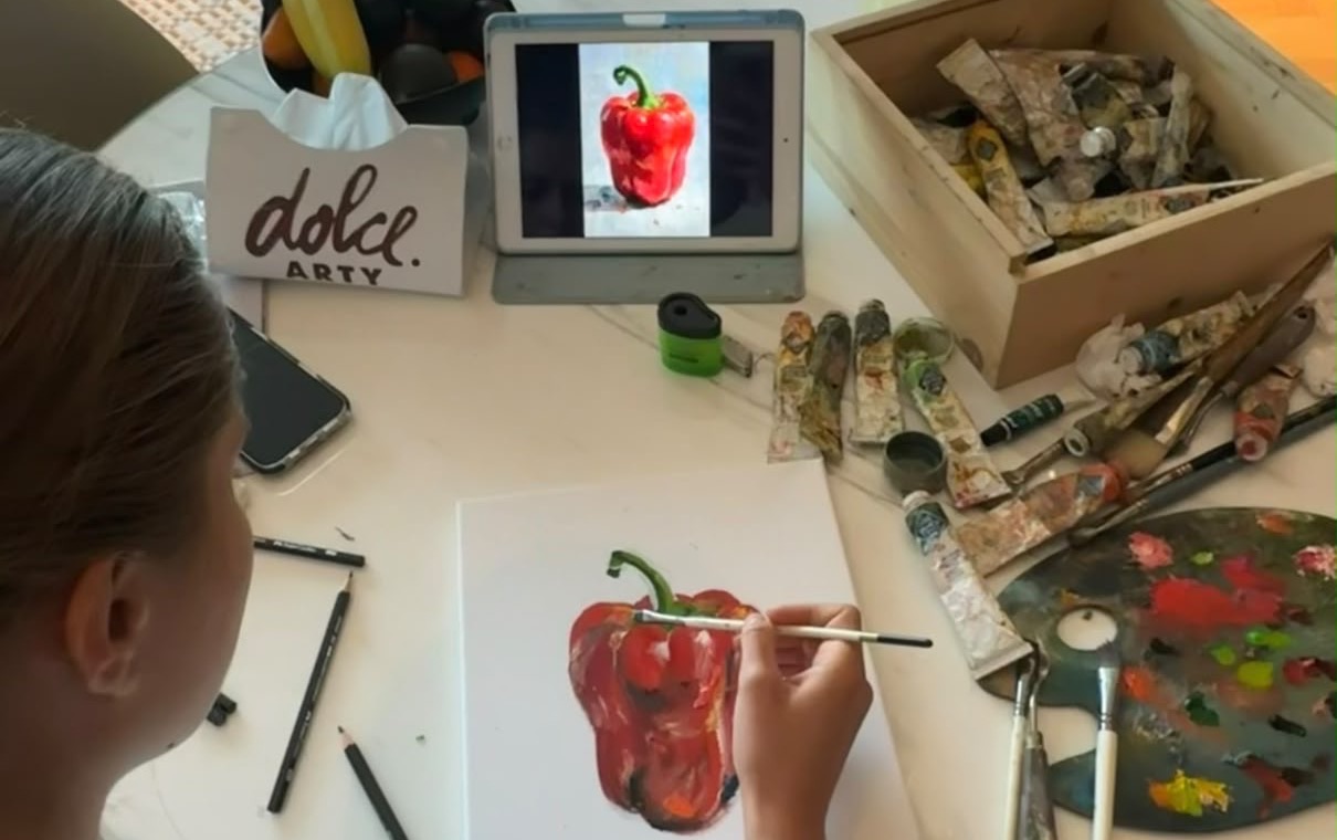 A student painting a red pepper in oil during a Dolce Arty session in Dubai, with brushes, palette and paints on the table