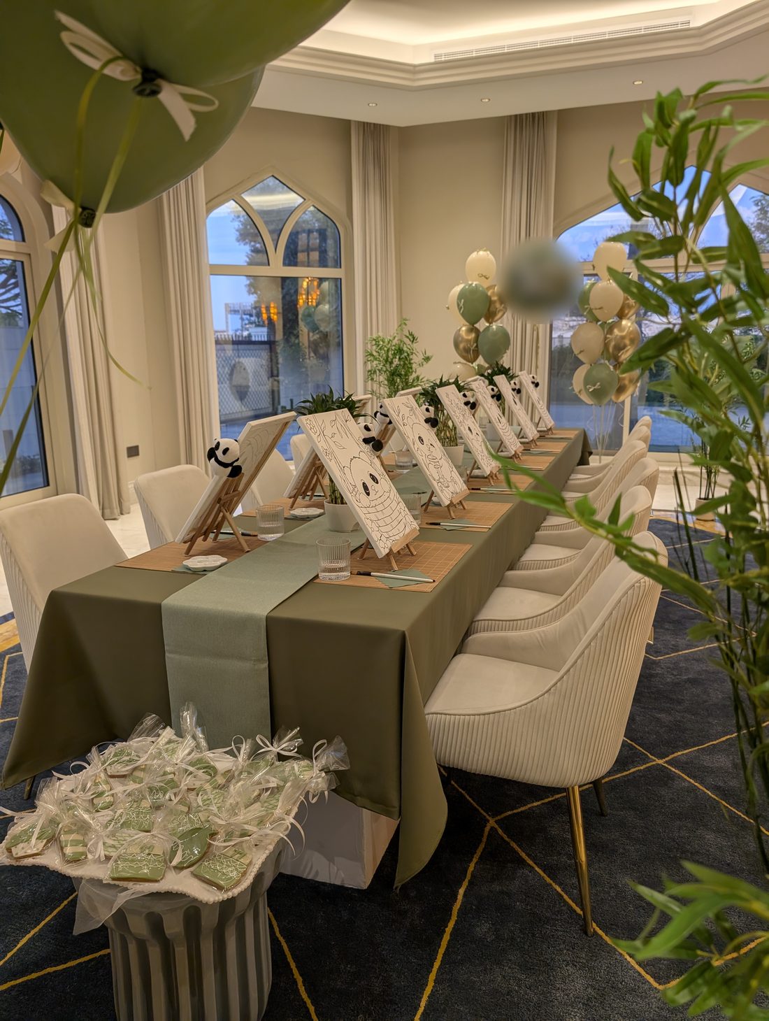 Panda canvases on tabletop easels along a sage green birthday table with bamboo placemats and lucky bamboo at a kids painting party in Dubai